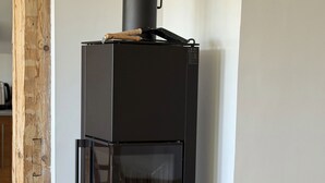 En modern vedkamin med en glaslucka, en korg med ved och ett runt träbord.