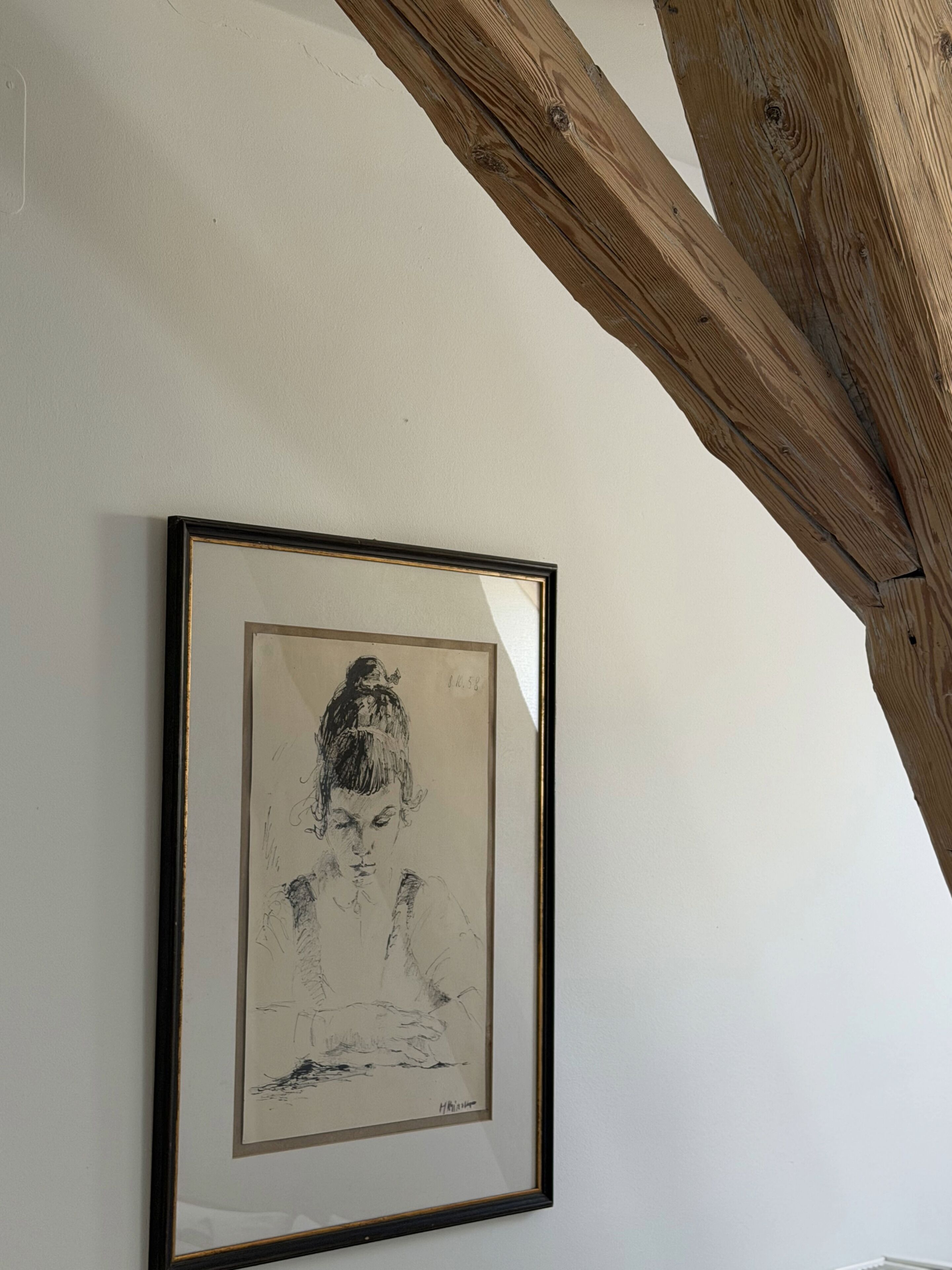 A framed black and white sketch on a white wall with a wooden beam above.