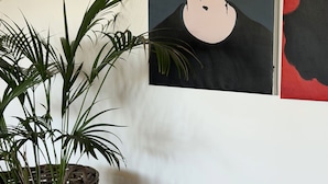 Ett rum med en flätad blomkruka, två randiga sittpuffar, ett vägguttag och en del av en affisch synlig.
