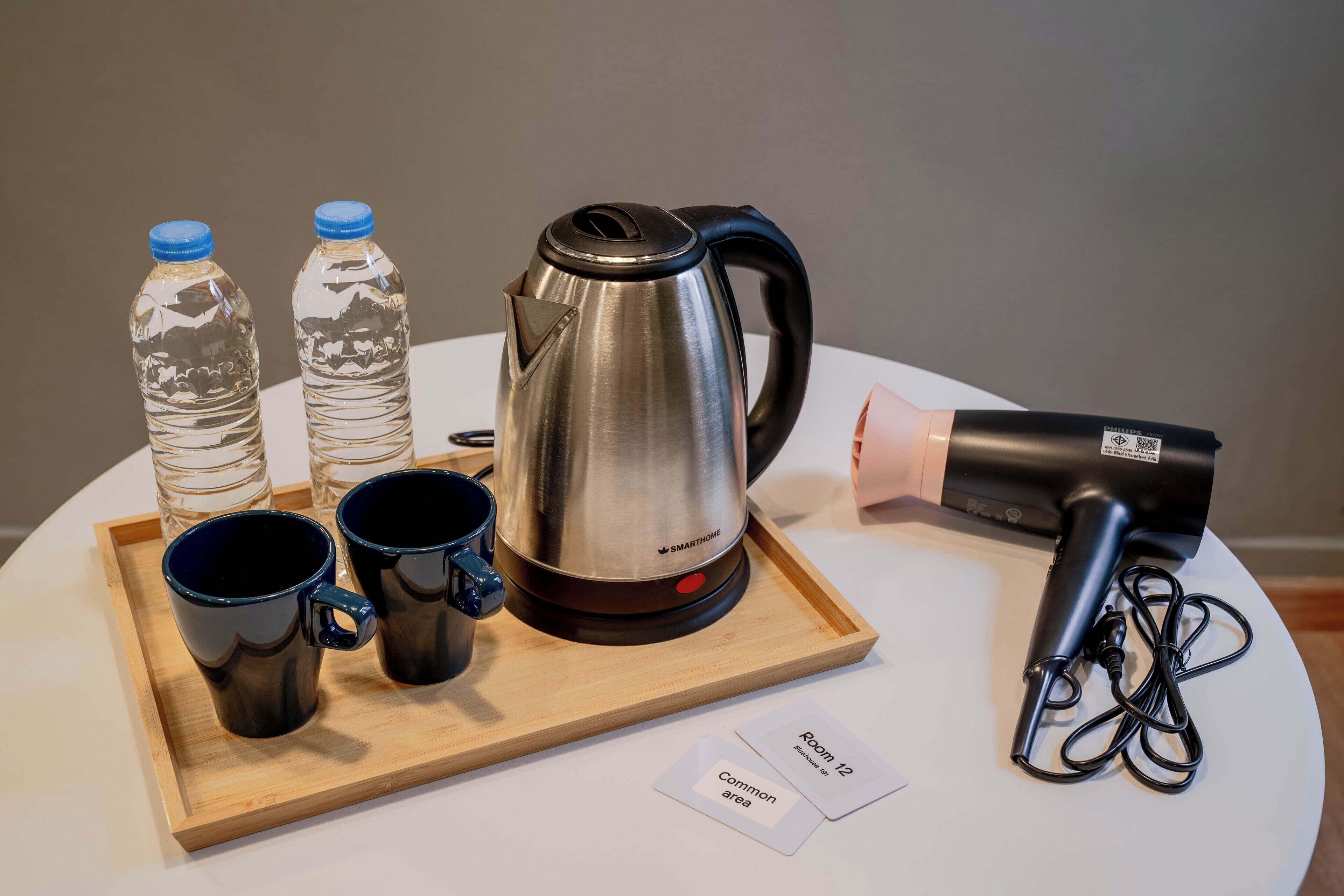 A tray with a stainless steel kettle, two water bottles, and two black mugs on a white table.