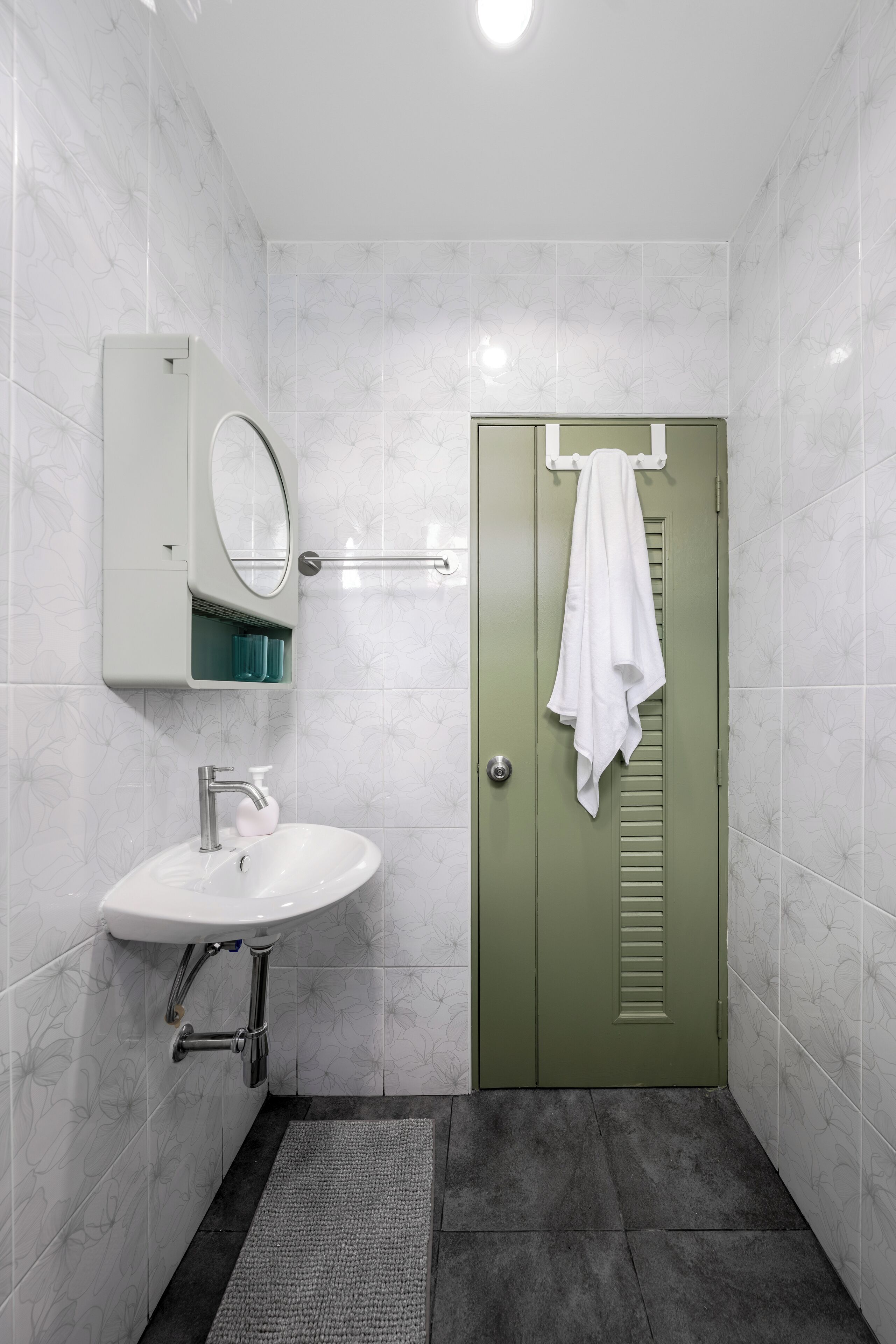 Une salle de bain avec un lavabo blanc, un miroir et une porte verte.