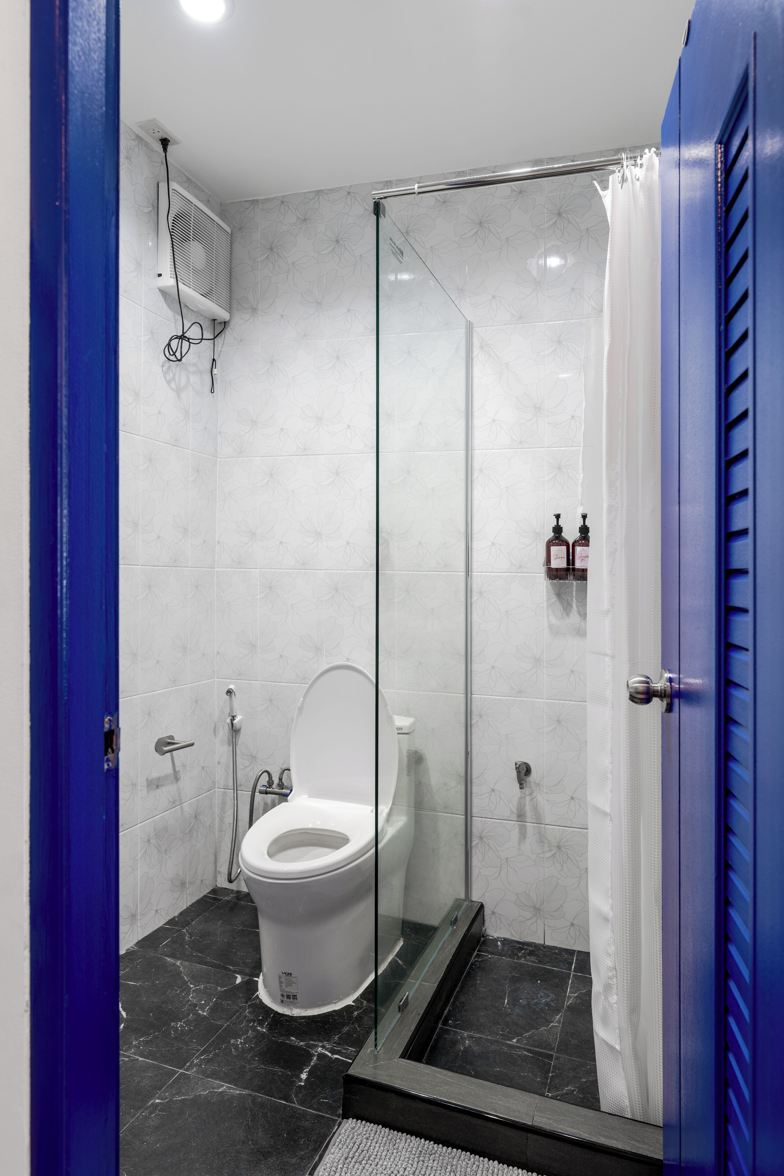 A modern bathroom with a glass-enclosed shower, a white toilet, and a blue door.