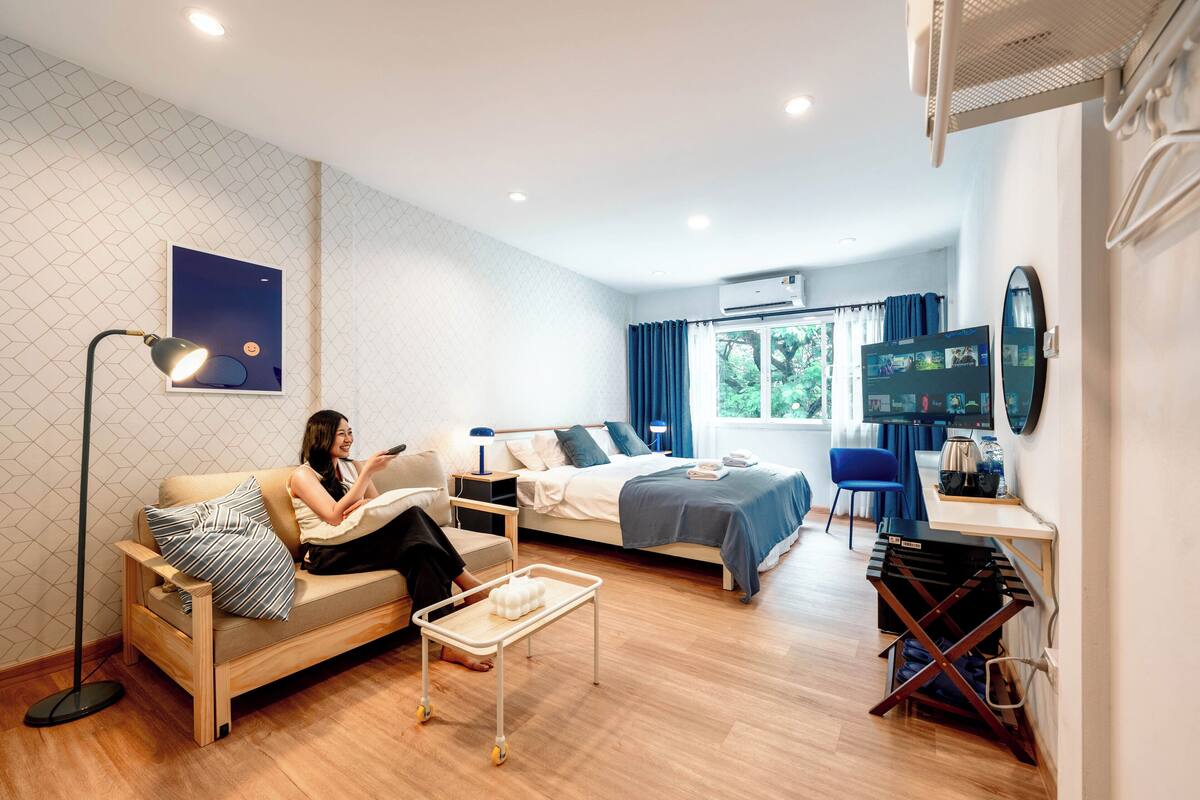 A modern hotel room with a sofa, a bed, a desk, and a TV.