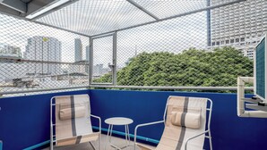 A balcony with two beige chairs and a small table, overlooking a cityscape with tall buildings and greenery. - Bluehouse191 hometel (Bangkok)