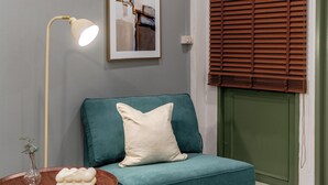 A teal sofa with a white pillow, a round wooden table with a vase, and a framed picture on the wall. - Bluehouse191 hometel (Bangkok)