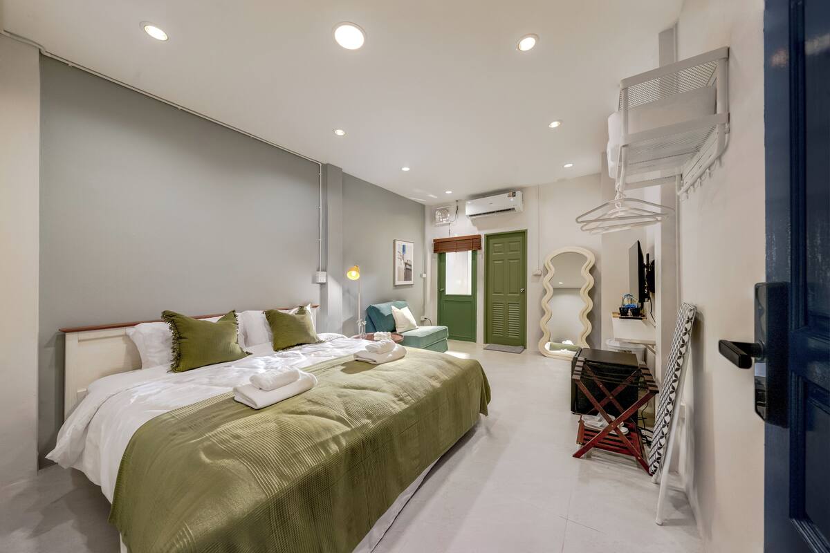 A modern bedroom with a large bed, a dresser, an ironing board, and a door with a mirror.