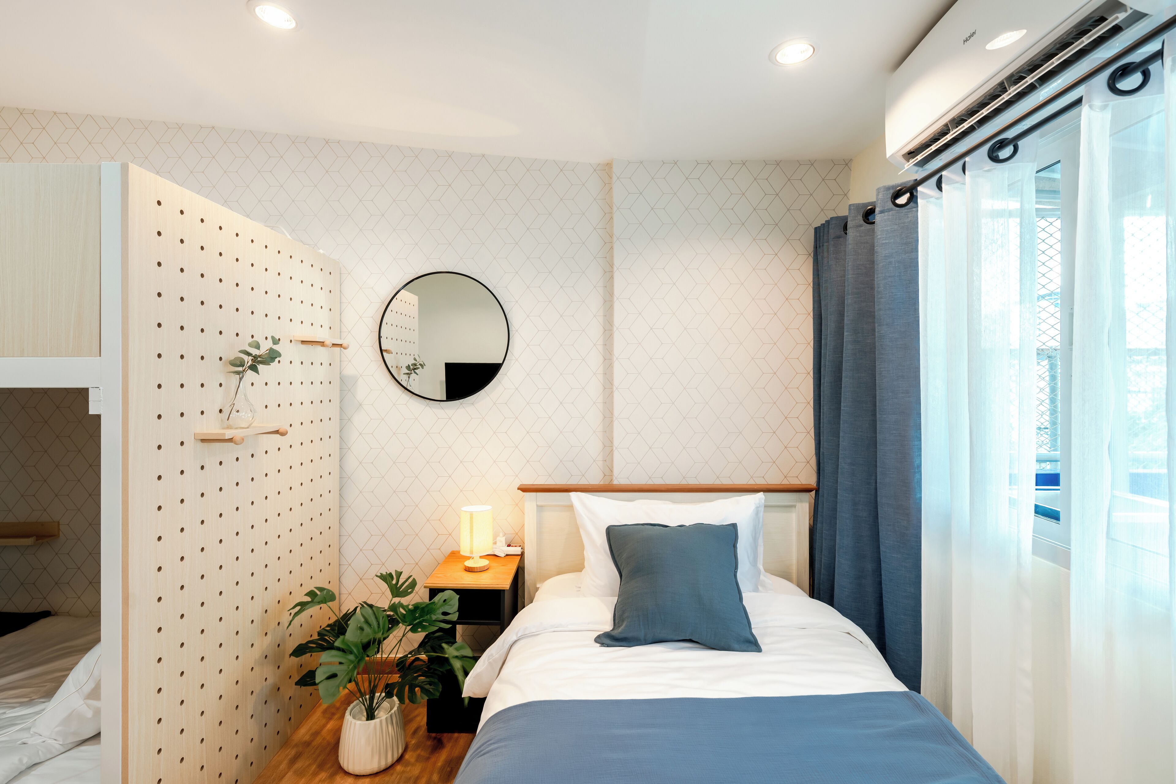 A modern bedroom with a bed, bedside table, mirror, and potted plants.