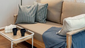 A cozy room with a sofa, a side table with two mugs, a floor lamp, and a wall-mounted picture. - Bluehouse191 hometel (Bangkok)