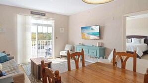 Una habitación acogedora con una mesa de comedor de madera, sillas, un sofá, un televisor y un cuadro de una playa.