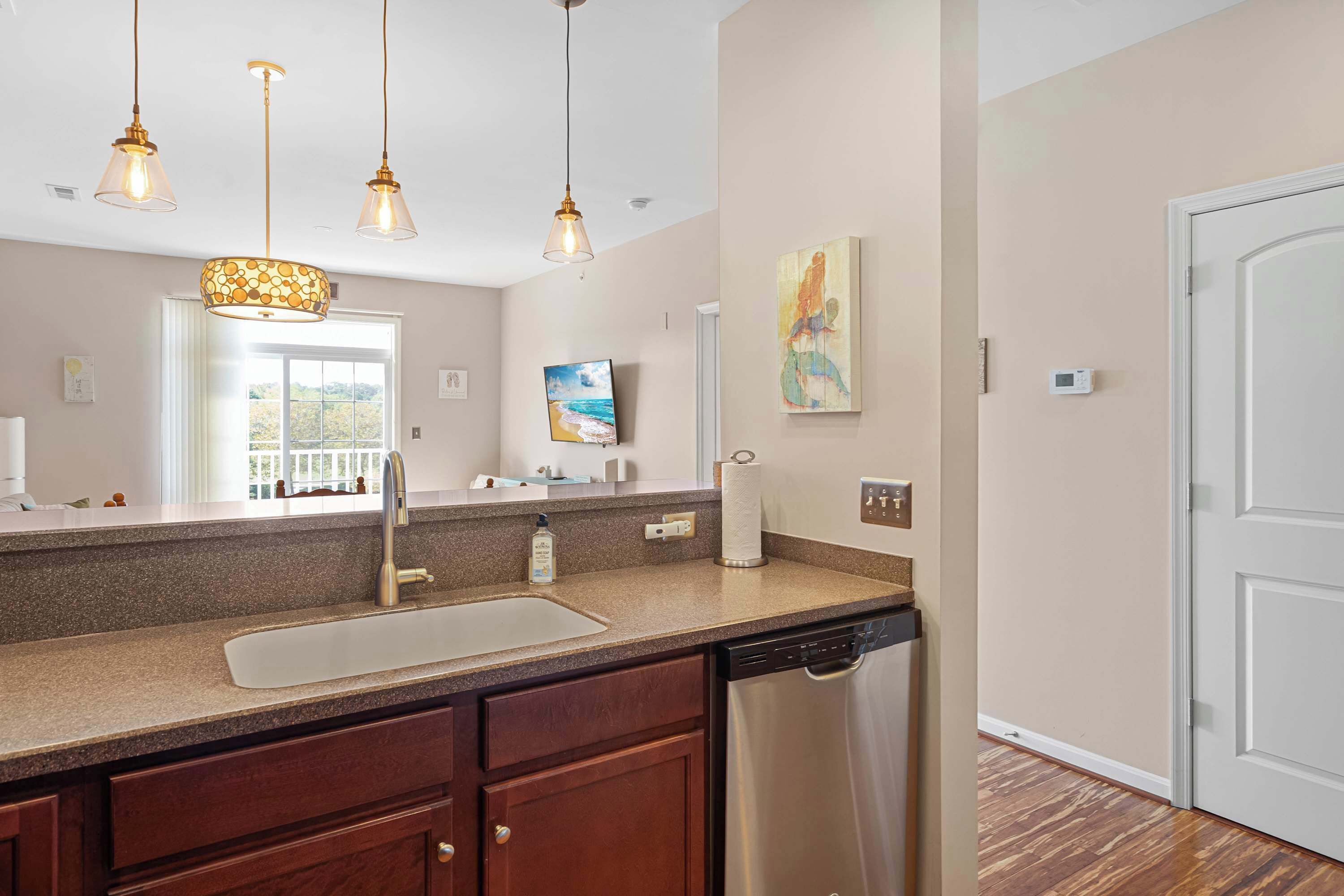 A kitchen with a granite countertop, stainless steel dishwasher, and pendant lighting.