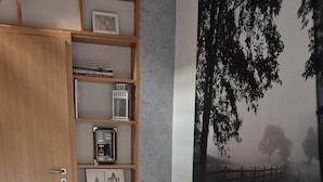 Una habitación con una mesa y sillas blancas, una estantería de madera y un amplio mural blanco y negro con un árbol en la pared.