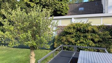 Eine Terrasse mit einem Metalltisch und Bänken, umgeben von üppigem Grün und einer Steinmauer.