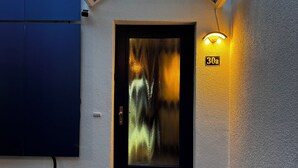 A building entrance with a glass door, a small outdoor light fixture, and a number sign indicating the unit. - Cozy vacation home in the heart of Cuxhaven (Cuxhaven)