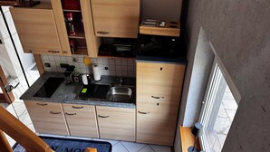 A compact kitchen with wooden cabinets, a built-in microwave, and a sink. - Cozy vacation home in the heart of Cuxhaven (Cuxhaven)