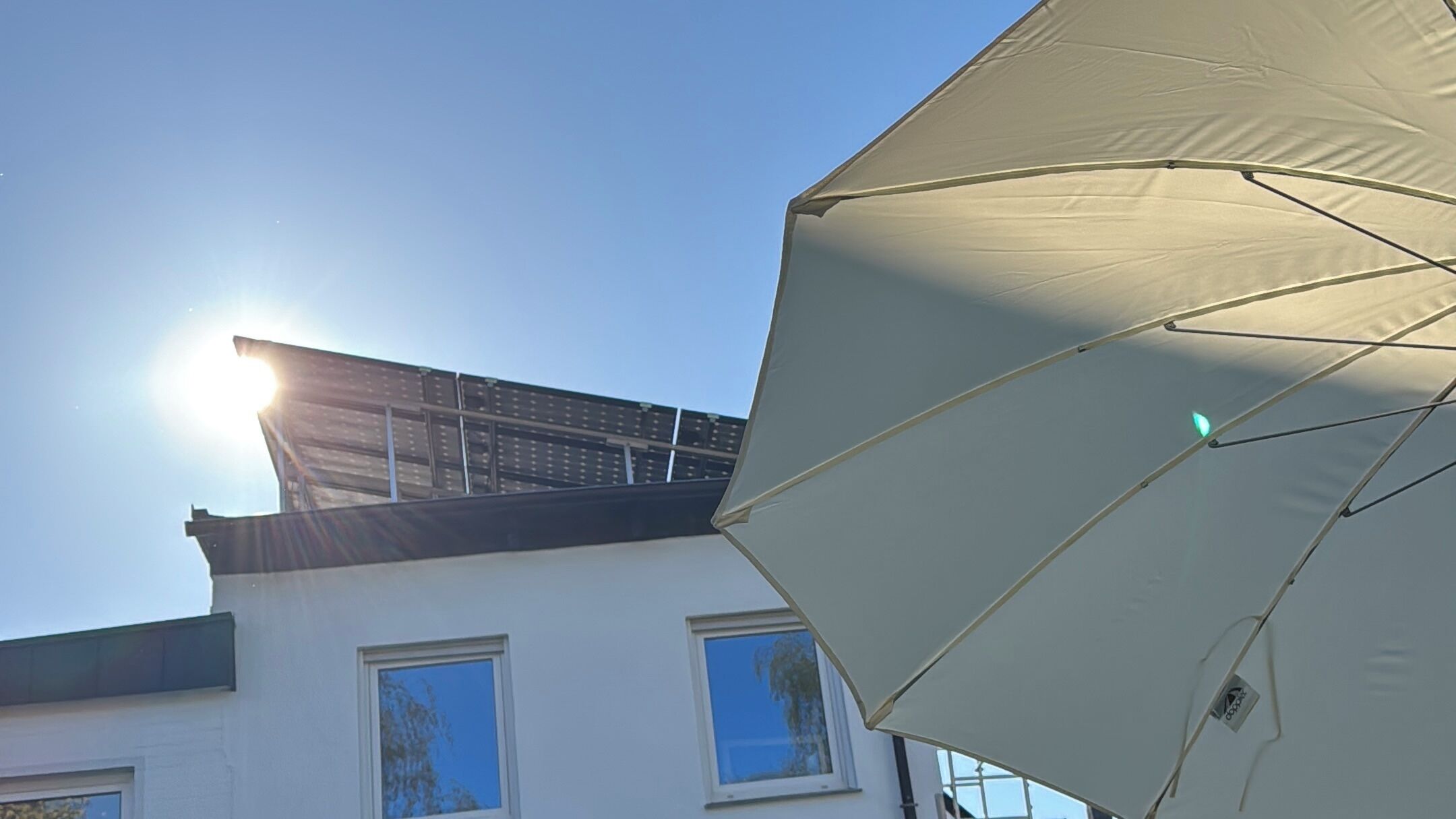 Een gebouw met een zonnepaneelinstallatie op het dak en een witte parasol op de voorgrond.