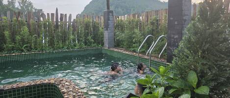 A swimming pool with a tiled edge, surrounded by greenery and a wooden fence.