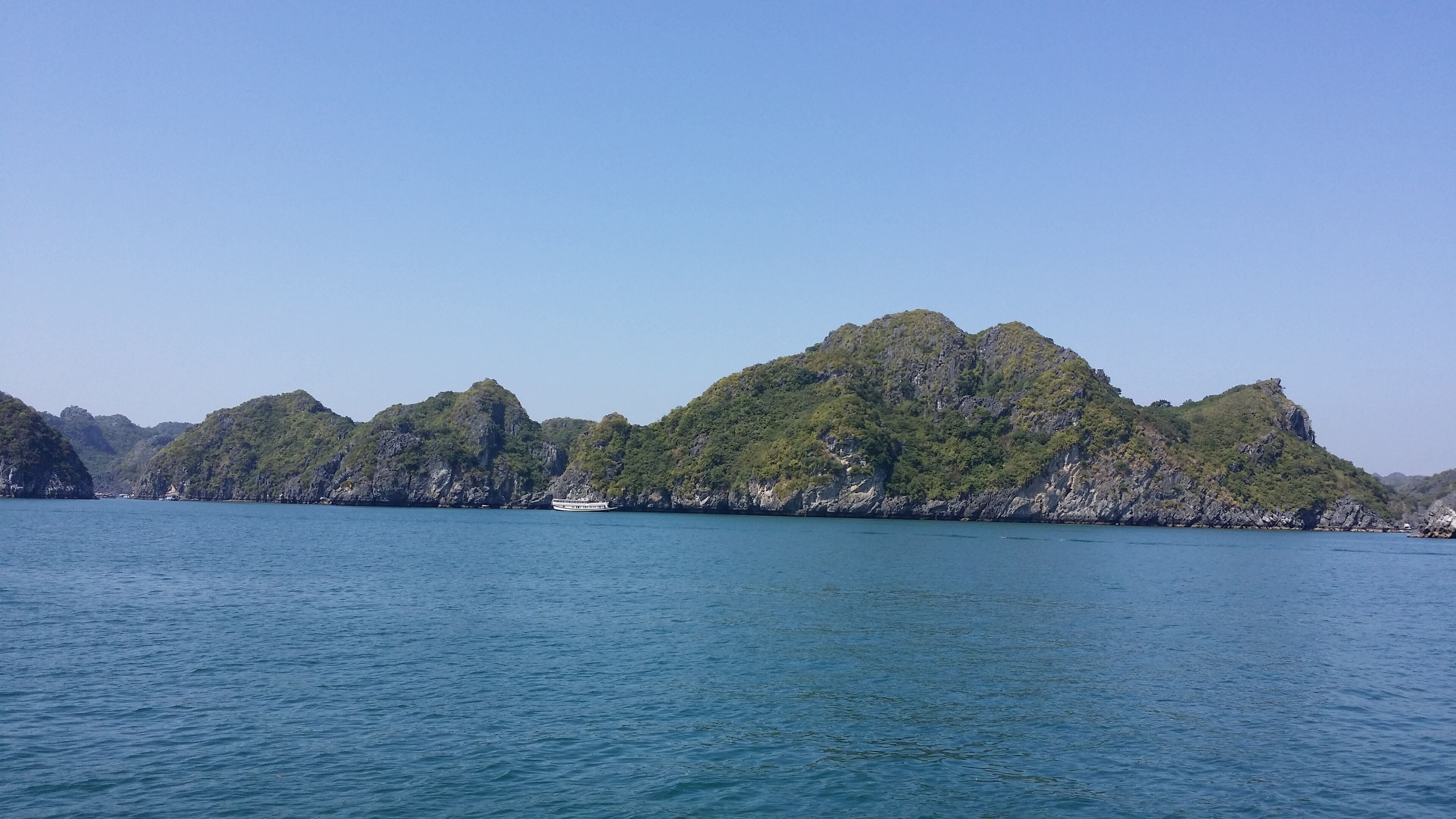 Un paisaje costero con un barco en el agua y una gran colina verde y boscosa al fondo.