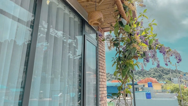 A building with large windows, a wooden ceiling, and a view of a hill with houses. - Shalva Homestay Catba (Hai Phong)