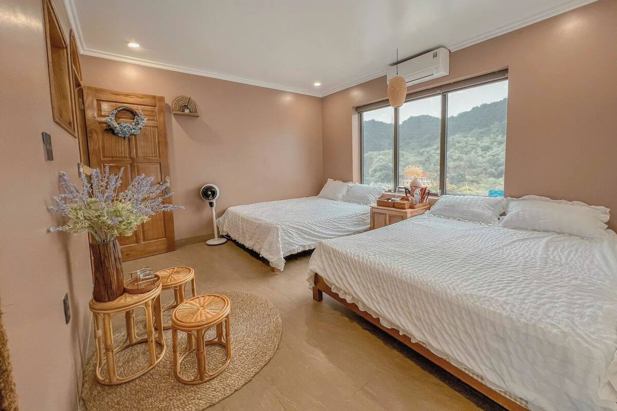 A bedroom with two beds, a wooden door, a window with a view, and a small table with chairs.