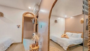 A bedroom with two beds, a mirror, a bedside table with a vase, and a small round table with a book. - Shalva Homestay Catba (Hai Phong)