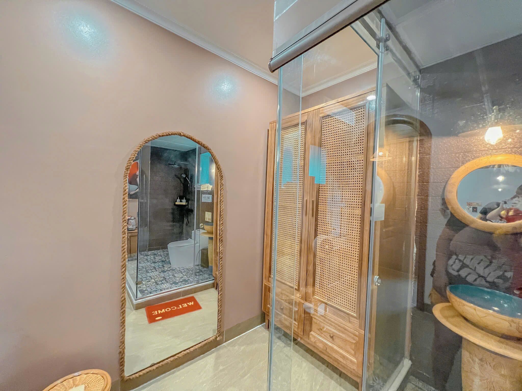 A bathroom with a glass shower enclosure, a wooden vanity with a perforated design, and a welcome mat.