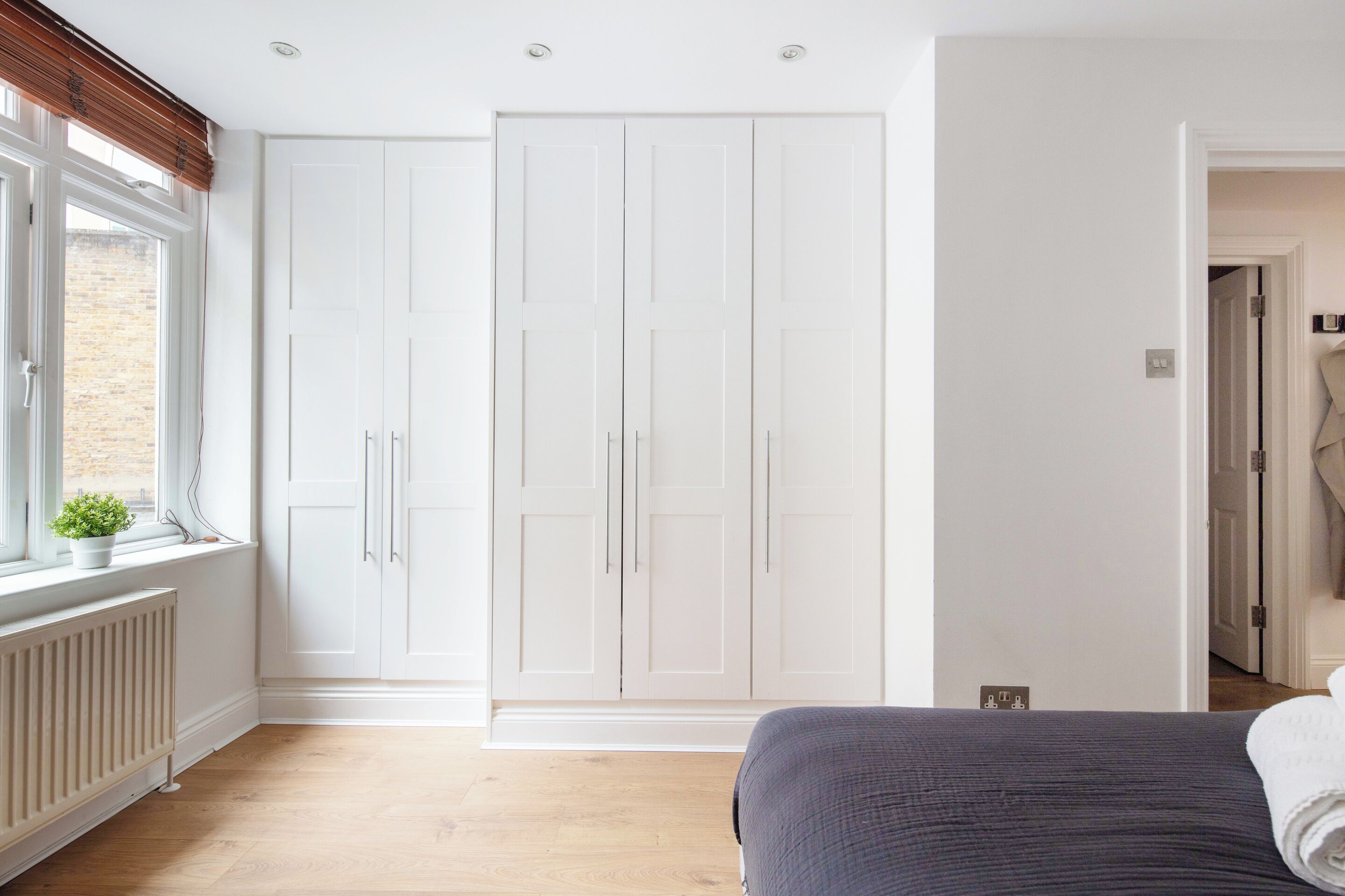 A bedroom with a large bed, a white wardrobe, and a window with blinds.