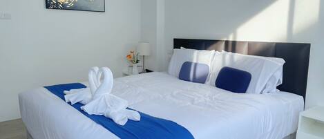A modern hotel room with a neatly made bed, a bedside table with a lamp, and a wall-mounted abstract painting.