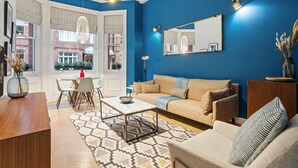 Un salon avec un mur bleu, un canapé beige, une table basse et un coin repas comprenant des chaises et une table.