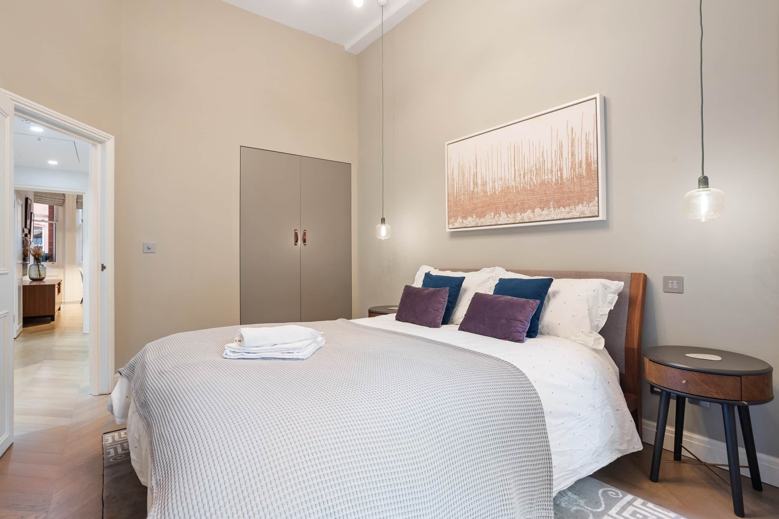 Une chambre à coucher avec un grand lit, une armoire, une table de chevet et un luminaire suspendu.