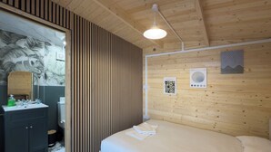 Een slaapkamer met een houten plafond, een bed met wit beddengoed, een houten hoofdbord, een spiegel, een wastafel met een groene fles en een behang met patroon.