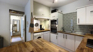 Een compacte keuken met een houten aanrecht, geïntegreerde apparatuur en een betegelde spatwand.