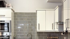 Een moderne keuken met witte kastjes, een grijze tegelachtergrond, roestvrijstalen apparatuur en een houten aanrecht.