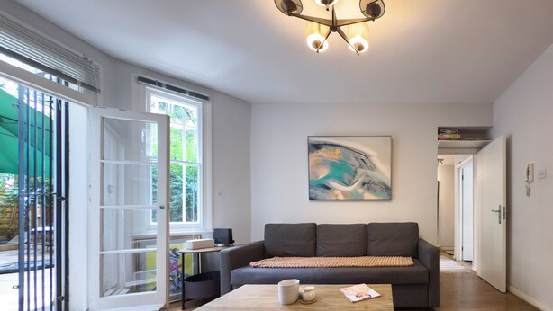 Een moderne woonkamer met een grijze bank, een houten salontafel en een groot abstract schilderij aan de muur.