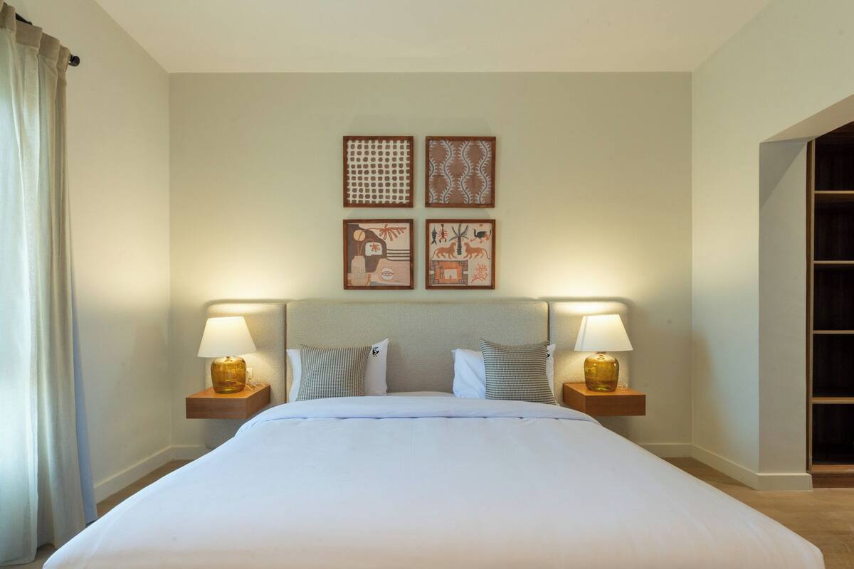 A hotel room with a large bed, two bedside tables with lamps, and two wall-mounted artworks.