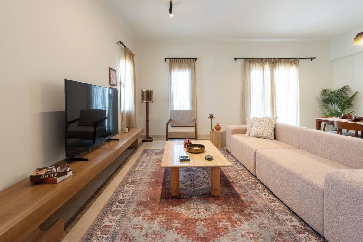 A living room with a TV, sofa, armchair, coffee table, and a patterned rug.