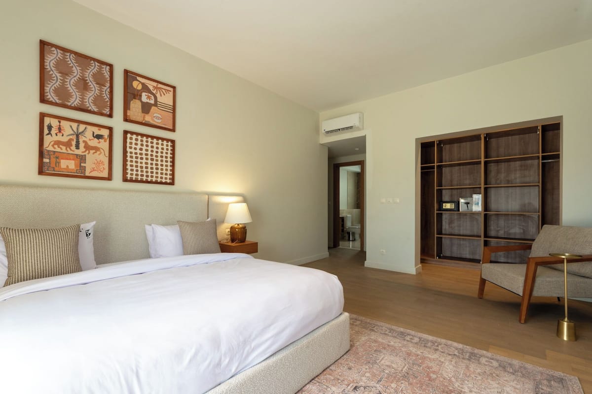 A hotel room with a large bed, a nightstand with a lamp, a wardrobe, and artwork on the wall.