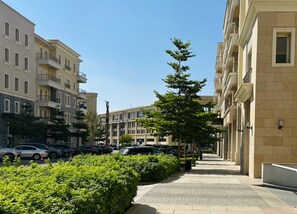 Un edificio residencial de varios pisos con balcones, una acera pavimentada y automóviles estacionados.