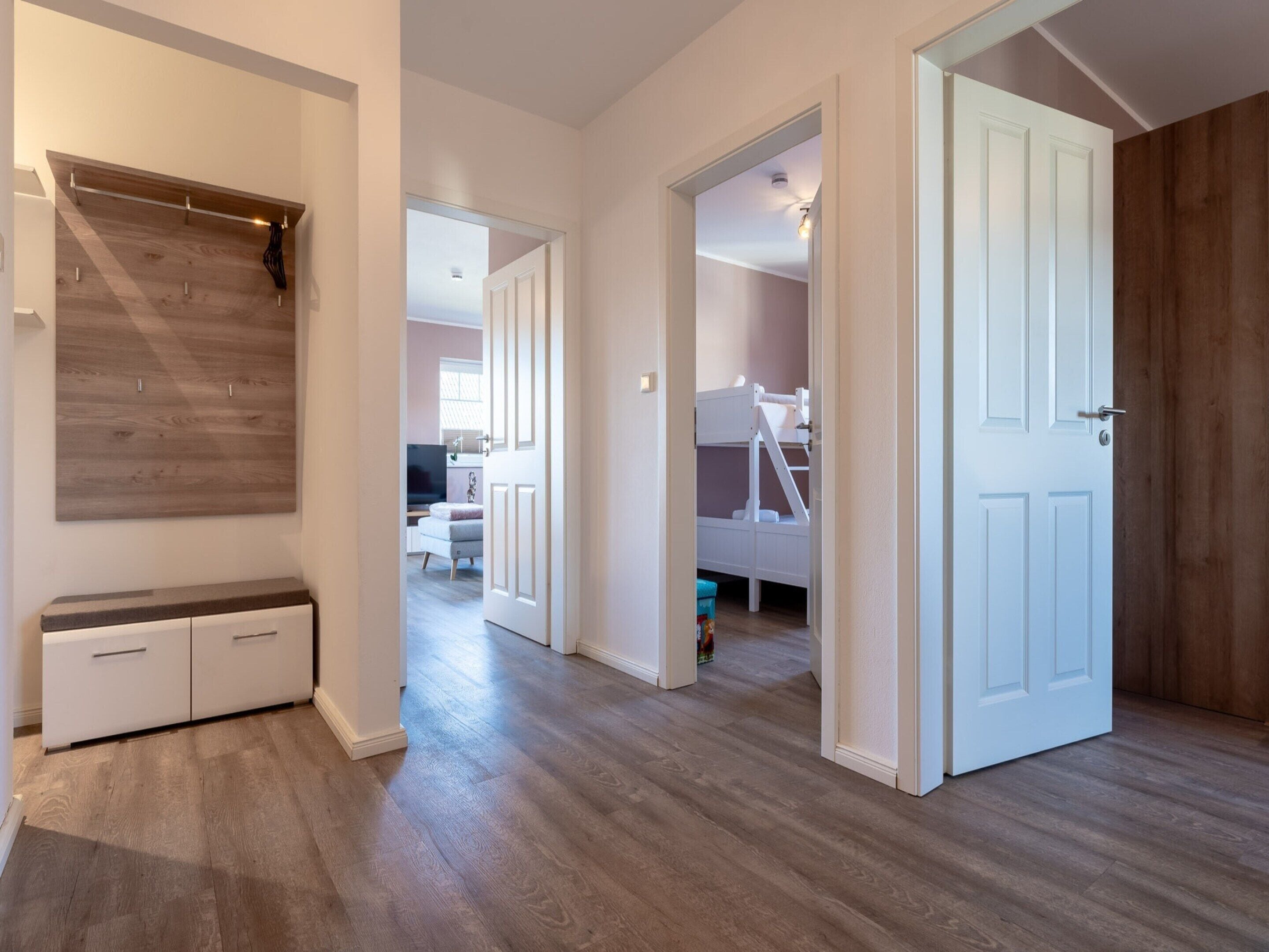 A hallway with a wooden floor, a bench, and a door leading to a room with a bunk bed.