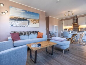 A modern living room with a sofa, coffee table, and a painting of a beach scene. - Ferienwohnung in St. Peter-ording (St. Peter-Ording)