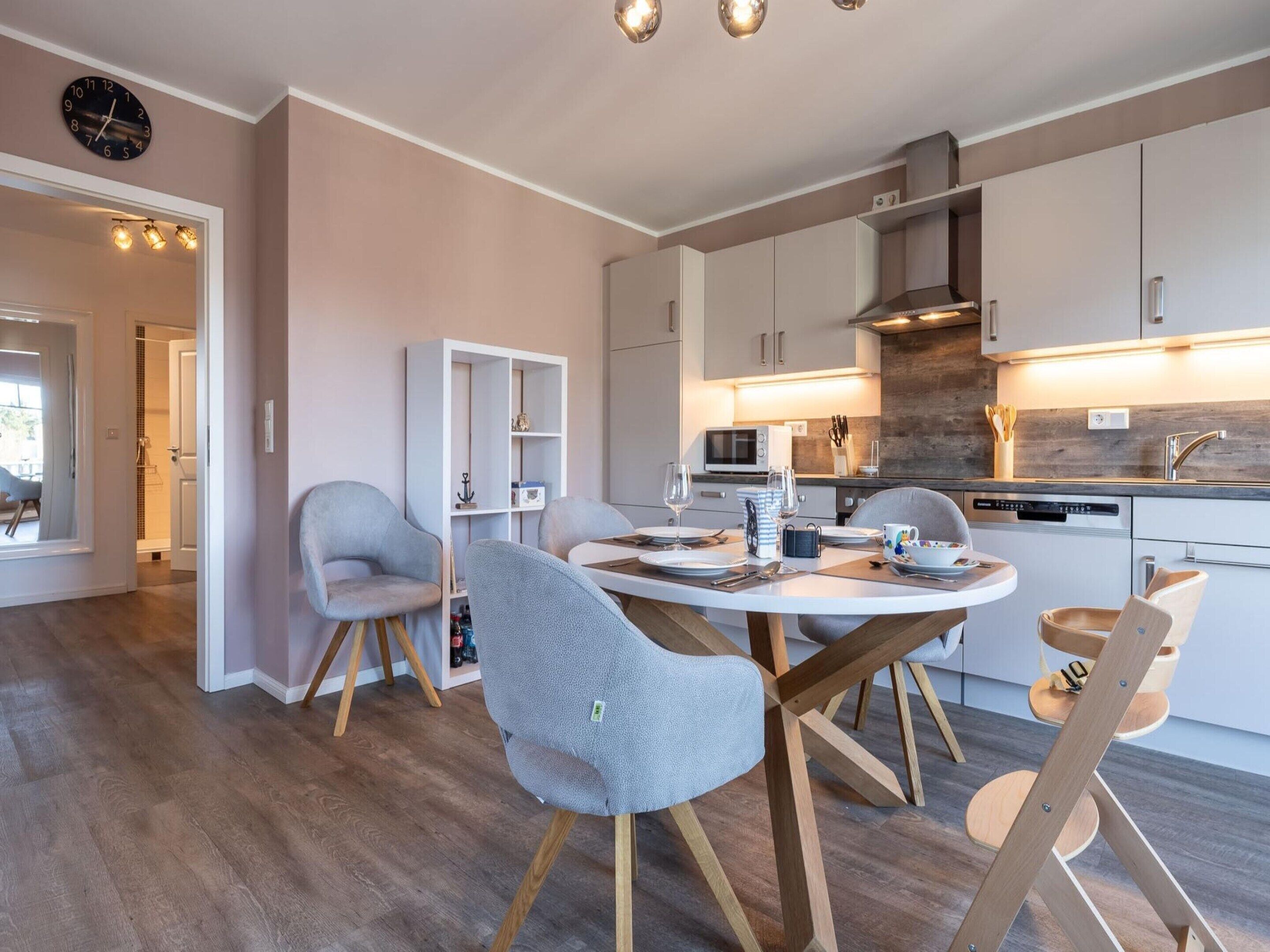 A modern kitchen with white cabinets, a microwave, and a dishwasher. There is a dining area with a round table and chairs.