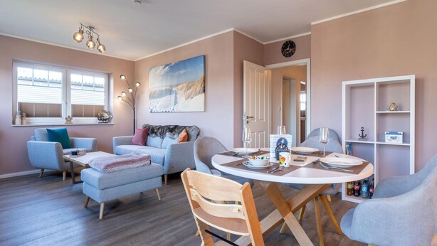 A modern living room with a dining area, featuring a sofa set, a wooden dining table with chairs, and a bookshelf. - Ferienwohnung in St. Peter-ording (St. Peter-Ording)