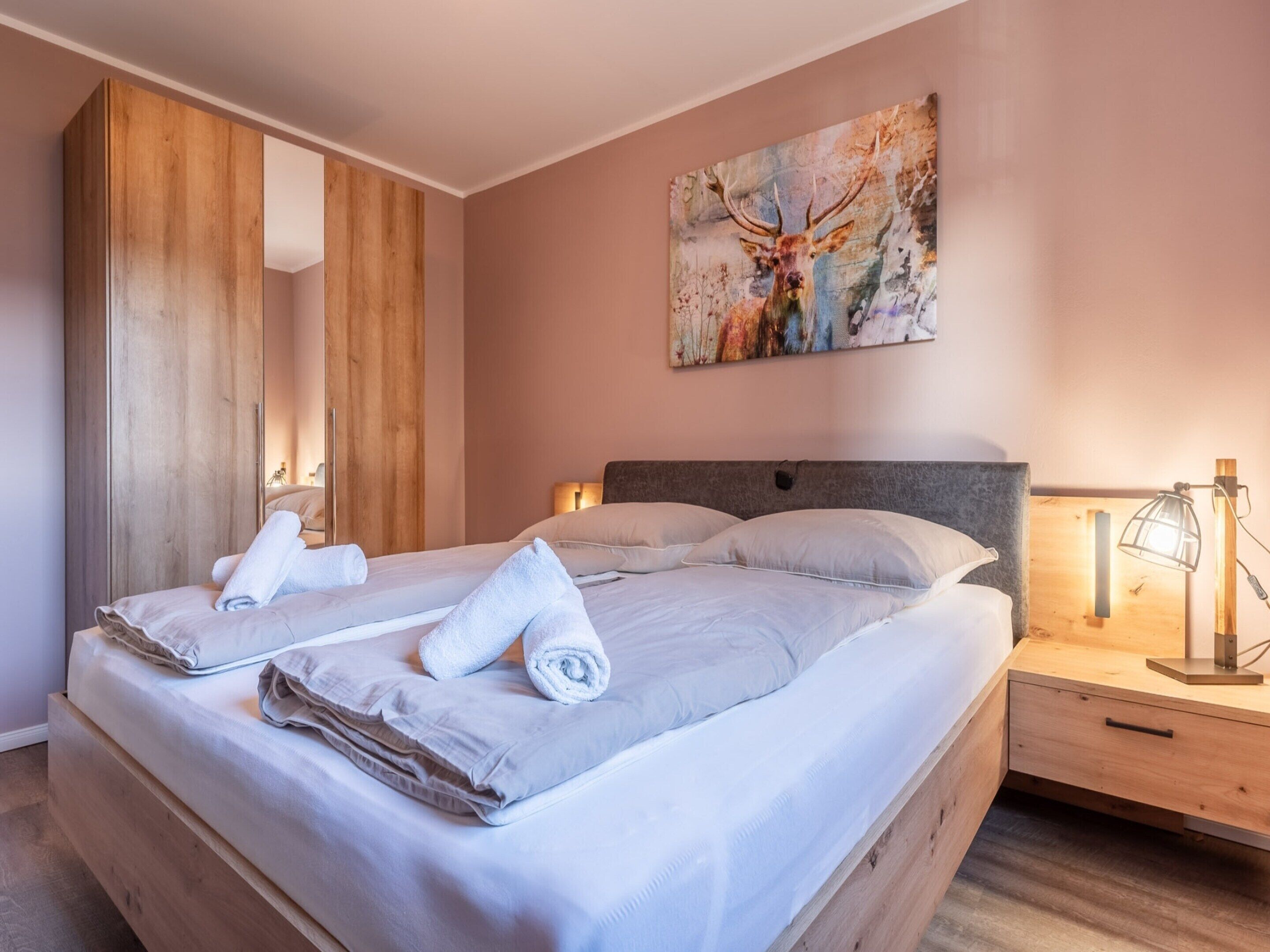 Een hotelkamer met een groot bed, een houten garderobe, een schilderij van een hert en een bedlamp.