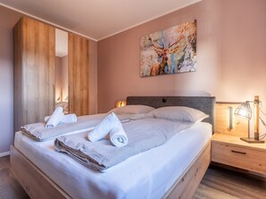 Et hotelværelse med en stor seng, et træskab, et billede af et dådyr og en sengebordlampe.