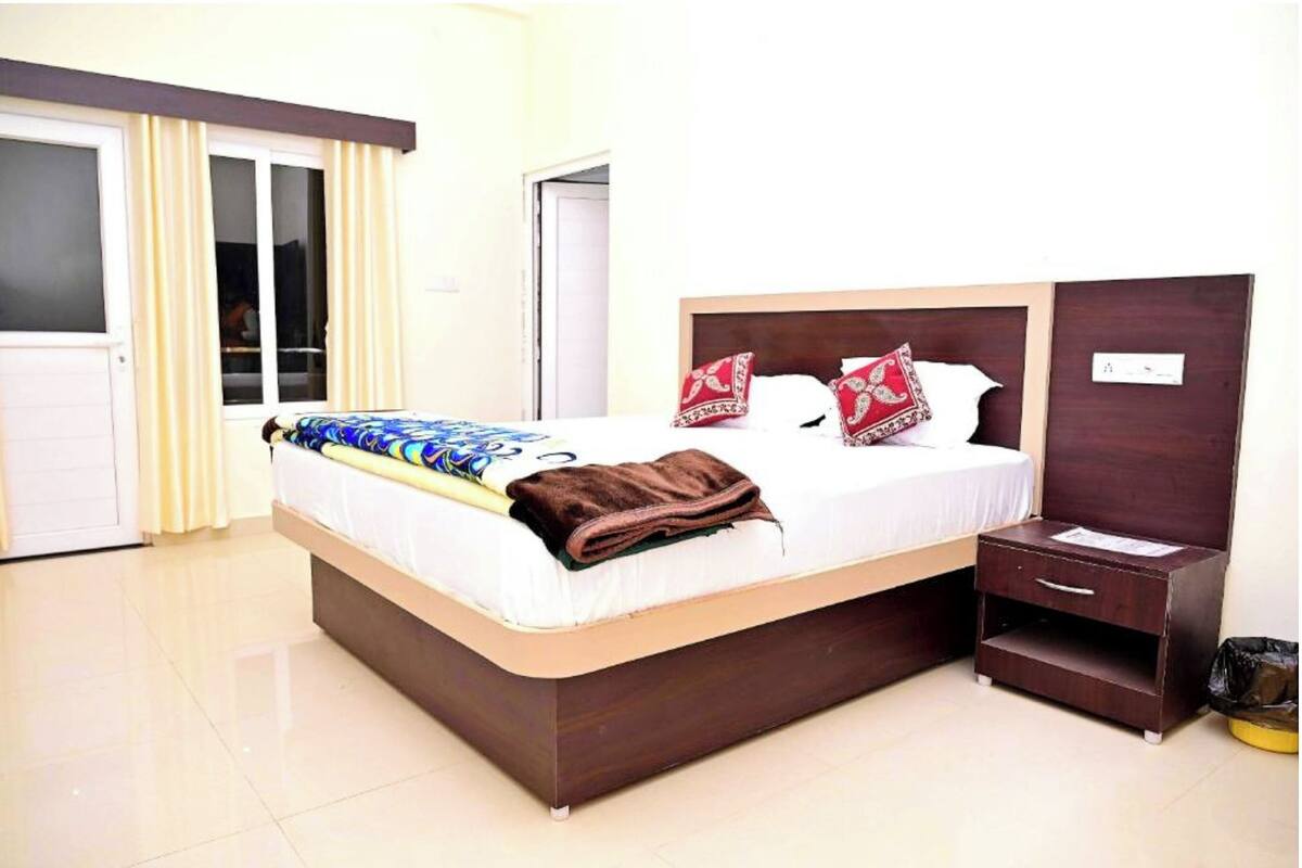 A neatly made bed with a brown blanket, a bedside table with a lamp, and a small drawer.