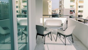 A balcony with a glass partition, white chairs, and a small table. - Family-Friendly 2BR Apt at Mackenzie Area, Pool available, 10 Min Walk to Beach! (Larnaka)