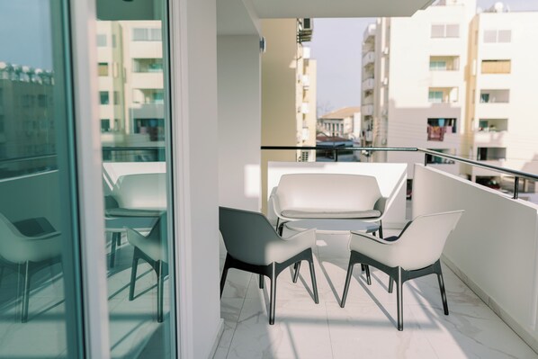 A balcony with a glass partition, white chairs, and a small table.