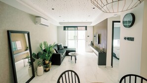 Un salon moderne comprenant un canapé, une table basse et des fauteuils, un coin repas avec une table et des chaises, et une cuisine avec un comptoir et des appareils électroménagers.