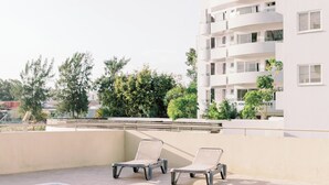 A swimming pool with two lounge chairs and a white building in the background. - Family-Friendly 2BR Apt at Mackenzie Area, Pool available, 10 Min Walk to Beach! (Larnaka)