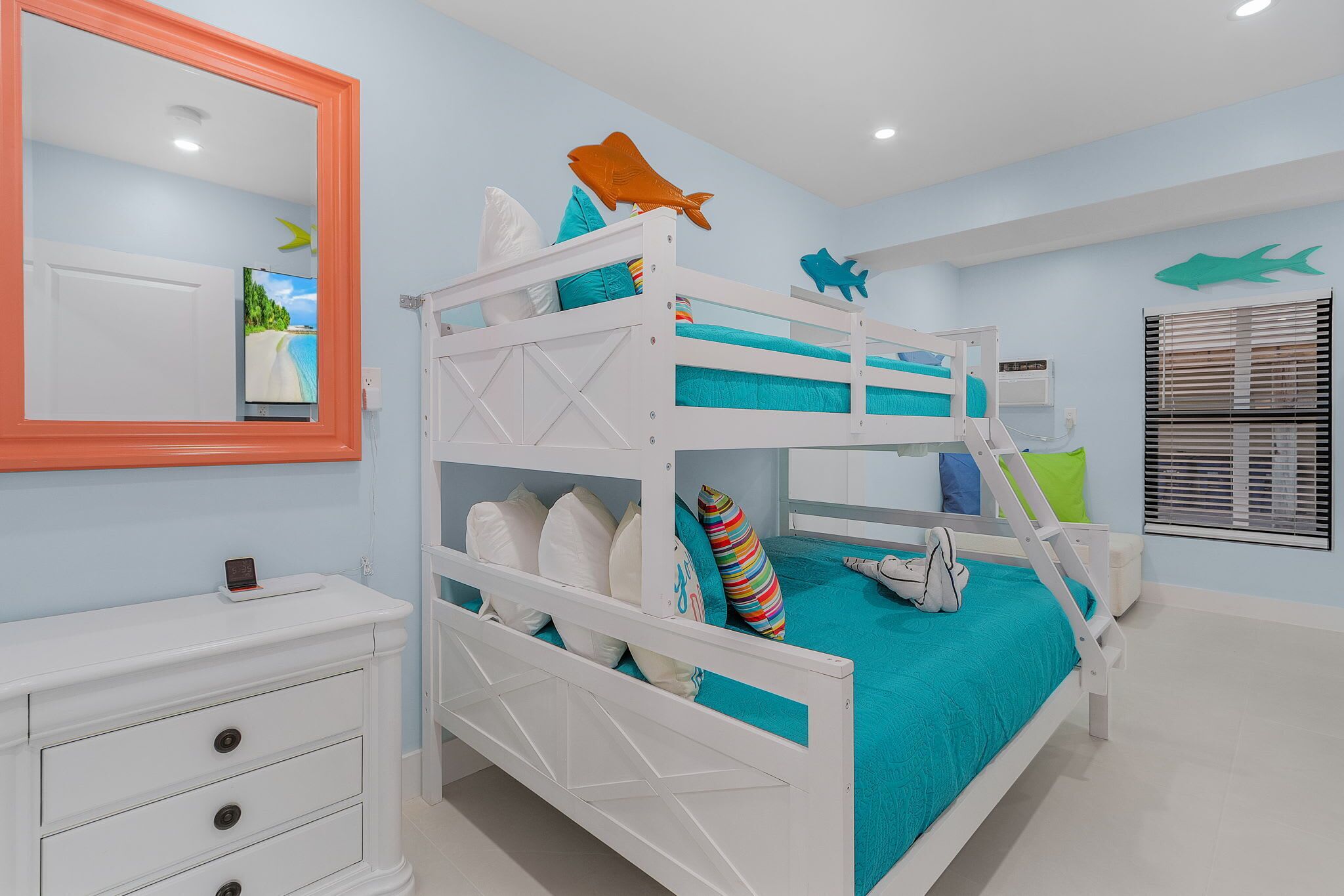 Una cama litera con estructura blanca, ropa de cama verde azulada y un espejo arriba.