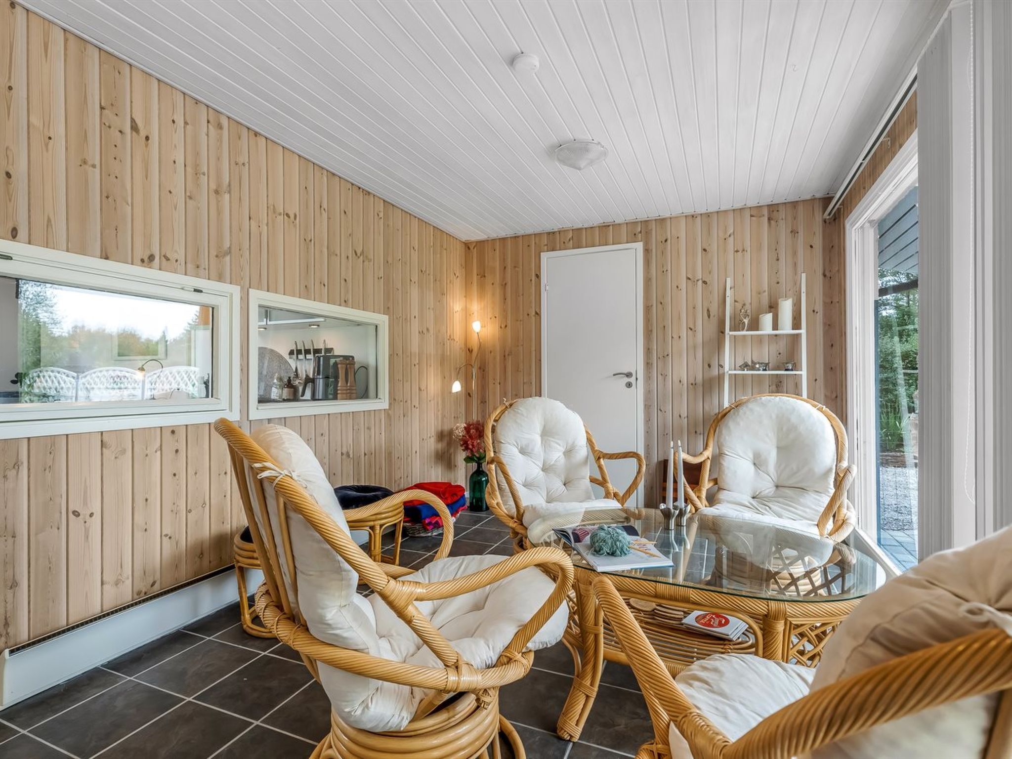 Una habitación acogedora con paredes de madera, una mesa de vidrio, sillas de mimbre y un espejo.